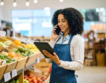 A shopkeeper taking an order on the phone while checking stock on a tablet