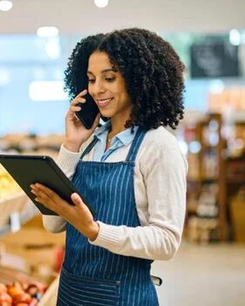 A shop owner taking an order on the phone with her stock list open on a tablet